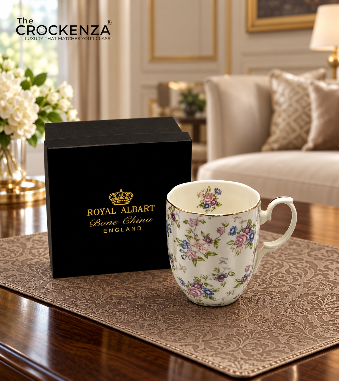 Royal Albart Bone Chana England ceramic mug with a floral pattern, displayed on a brown patterned placemat next to its black gift box on a wooden table in a cozy living room setting.